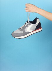 Hand holding gray sneaker by the laces on blue background
