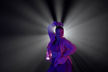 Girl in pink clothes dancing in dark studio with smoke and backlight. The dancer demonstrates...