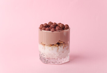 Homemade layered Desserts in a glass cups with yogurt and chocolate balls on a pink background