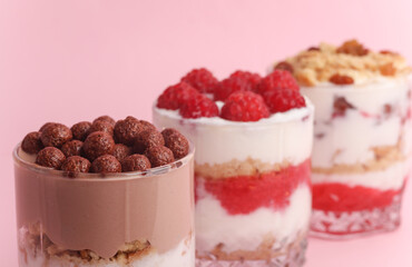 Homemade layered Desserts in a glass cups with yogurt, berries, cookie and chocolate on a pink background