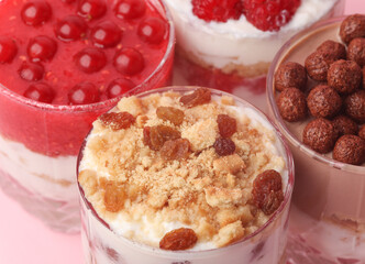 Homemade layered Desserts in a glass cups with yogurt, berries, cookie and chocolate on a pink background