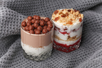 Homemade layered Desserts in a glass cups with yogurt, cookies and chocolate balls on gray fabric blanket