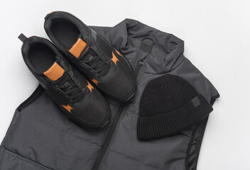 Men's sleeveless down jacket, sneakers and hat on a white background. Top view. Sportswear.