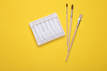 Set of white empty tubes of acrylic or oil paint and brushes for creativity on yellow background. Template for design, mockup