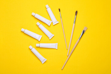 Set of white empty tubes of acrylic or oil paint and brushes for creativity on yellow background. Template for design, mockup