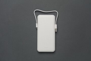 White power bank with cable on dark gray background. External battery for charging smartphone and...