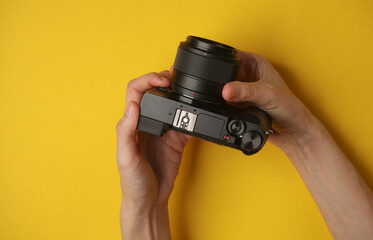 Hands holding a modern mirrorless camera on yellow background