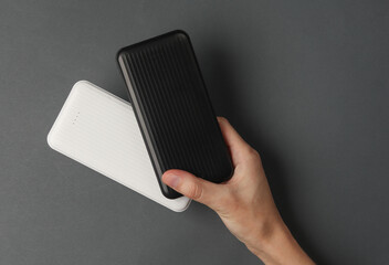 Hand holding white and black external battery power banks on a dark gray background