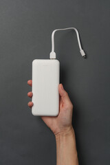 Hands holding white external battery power bank on a dark gray background