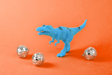 Toy dinosaur tyrannosaurus rex with party disco balls on a orange background. Minimalism creative...