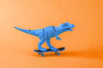 Toy dinosaur tyrannosaurus rex with skateboard on orange background. Minimalism creative layout