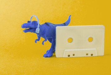 Toy dinosaur tyrannosaurus rex with headphones and audio cassette on yellow background. Minimalism creative layout. Music lover. Retro 80s