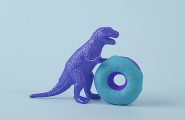 Toy dinosaur tyrannosaurus rex with donut on blue background. Minimalism creative layout