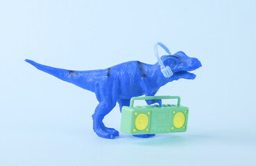 Toy dinosaur tyrannosaurus rex with boombox audio player and headphones on blue background. Minimalism creative layout