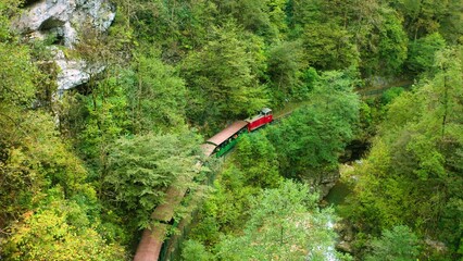 A Tourist Train with Tourists Travels along a Narrow-gauge Railway through a Mountain Gorge...