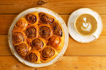 Homemade cinnamon rolls from yeast dough and cup of coffee cappuccino on wooden table. Top view.