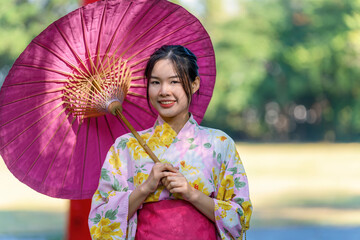 A young woman wearing a Japanese traditional kimono or yukata holding an umbrella is happy and...