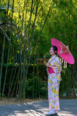 A young woman wearing a Japanese traditional kimono or yukata holding an umbrella is happy and...