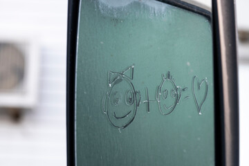 Reflection in the car mirror of glass with frost on which emoticons are drawn with the meaning of boy plus girl, different love.
