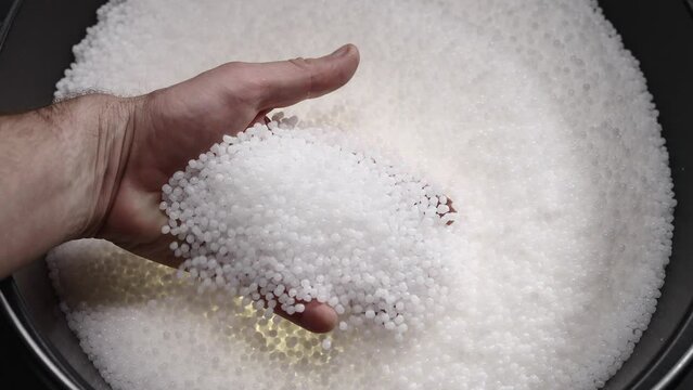 A factory worker checks plastic pellets before they are put into production. White compound in a man's hand. Production