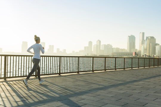 Senior fitness woman jogging on seafront promenade in sunshine morning. Healthy lifestyle, sport, active life in city.