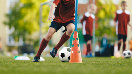 Youth in sports training. Player kicking ball during a soccer training drill. Slalom practice for football players. Summer sports practice camp for school kids - obrazy, fototapety, plakaty