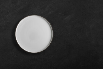 Obraz na płótnie Canvas Handmade empty ceramic plate top view with copy space on dark concrete table. Minimalism. Eco friendly ceramics handcraft tableware.