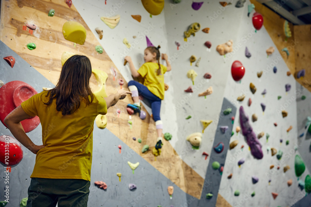 Wall mural female bouldering trainer teaching little girl, child bouldering activity, techniques. little girl c