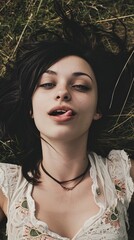 young lively woman, black hair, romantic expression on her face, she is sticking her tongue out, laying on the grass