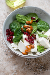 Salad with fresh spinach, feta cheese, pomegranate seeds and almonds, vertical shot on a beige granite surface, middle closeup