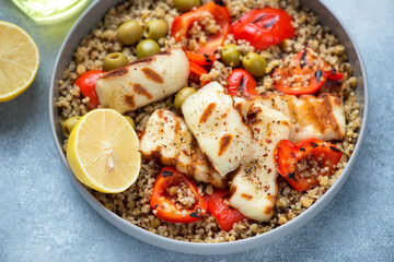Quinoa with grilled halloumi cheese, red bell pepper and green olives, horizontal shot on a light-blue stone background, middle closeup