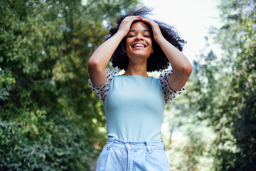 Happy african american teen girl in casual cloth. Smiling darkskin female teenager walking in the par - obrazy, fototapety, plakaty