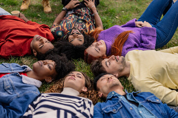 group of young multiethnic people lying in a circle on the grass with their eyes closed