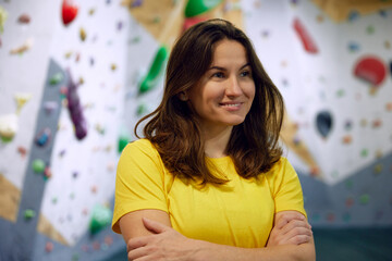 Portrait of young smiling woman in yellow t-shirt, bouldering instructor standing with climbing...