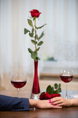 A red rose in a vase stands on a wooden table.
