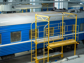 Modern blue train carriage prepared for painting in repair shop, yellow scaffolding along carriage