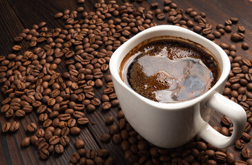white cup of coffee with beans on a dark wood table