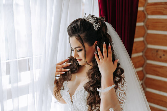 A wonderful beautiful portrait of a young bride. Beautiful bride with wedding makeup and jewelry wreath on long curly hair. Wedding photo model with brown eyes in a beautiful interior.