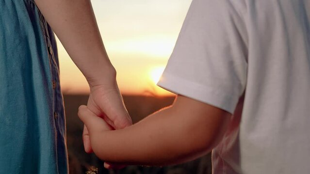 Child and mother share hands in front of sun. Closeup mother lets go of child hand, separation. Separation of hands of mother and son. Family at sunset. Separation, parting, quarrel. Misunderstanding