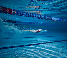 Underwater swimming. Young girl in red swimsuit, cap and goggles training, practicing, swimming in pool indoors. Concept of pool sports, water sport, competition, active lifestyle