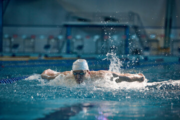 Butterfly swimming techniques. Athletic young man in motion, training, swimming in pool, wearing...