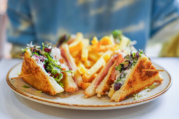 Club sandwich with ham, cheese, lettuce, and fries on the side.