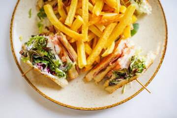 Overhead view of a club sandwich with fries and fresh greens.