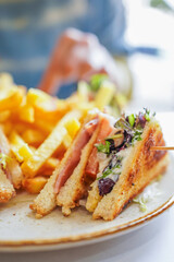 Sandwich with ham and lettuce served with fries on a ceramic plate.