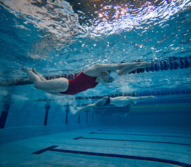 Underwater swimming. Young girl in red swimsuit, cap and goggles training, practicing, swimming in pool indoors. Concept of pool sports, water sport, competition, active lifestyle