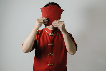 Asian man wearing Cheongsam or Chinese traditional cloth is covering his face with angpao or red...