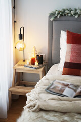 Bedside table with lamp and candles next to a bed with pillows and blanket