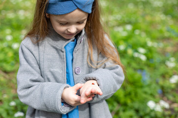Adorable little girl wearing blue linen dress with ladybug among first spring flowers. soft focus
