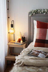 Bedside table with lamp and candles next to a bed with pillows and blanket