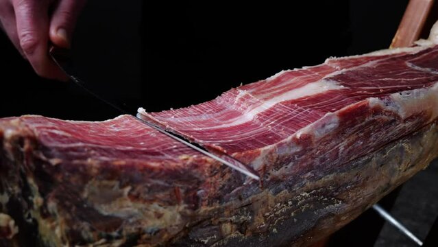 Man cutting slicing a traditional Iberico Spanish ham, jamon. Whole leg. Close up
